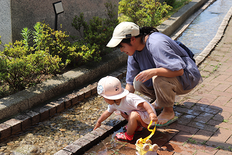 せせらぎの水に触れる親子の写真