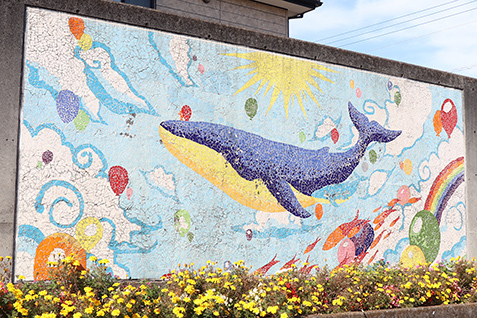 写真：大師通りにあるポケットパークの壁画。くじらが太陽や雲、風船とともにタイルで描かれている。
