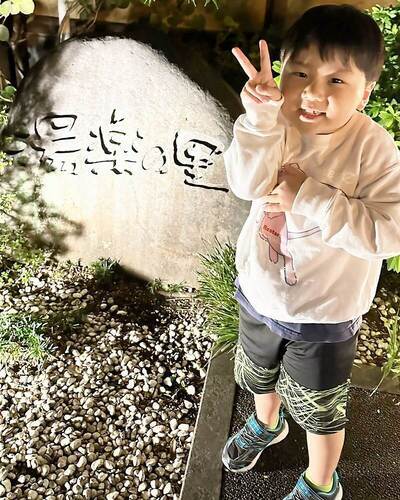 画像：入浴施設の看板の前で男の子がピースをしている