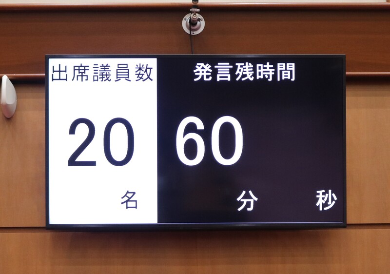 議場内の大型モニターに出席議員数と発言残時間が映し出されている写真