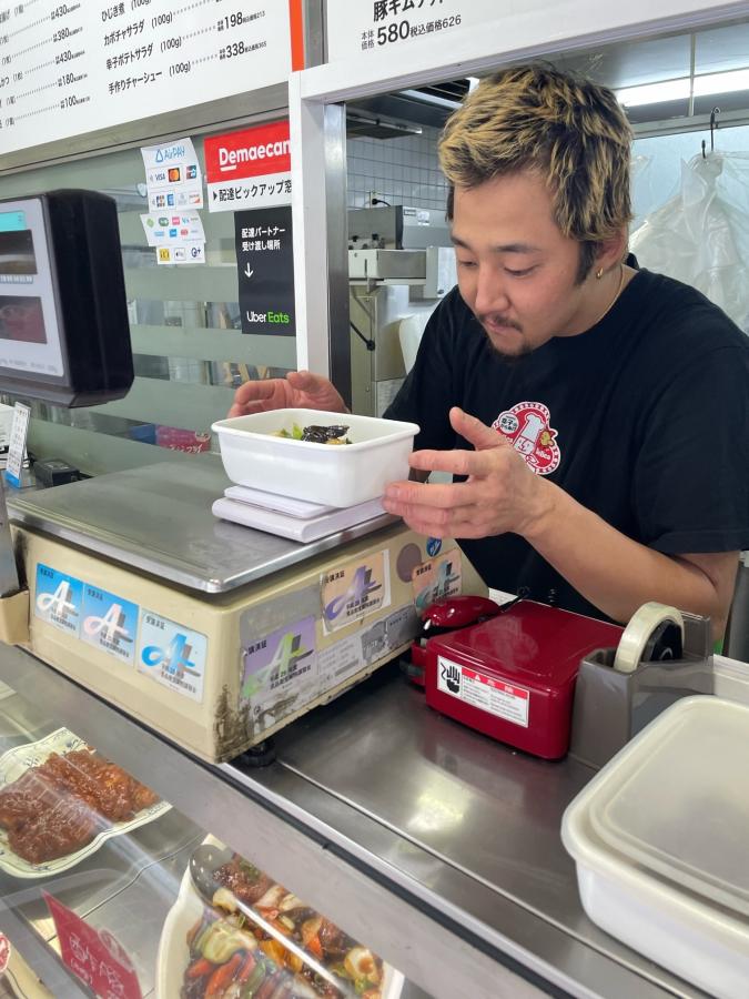 持参容器にお惣菜を入れる店長